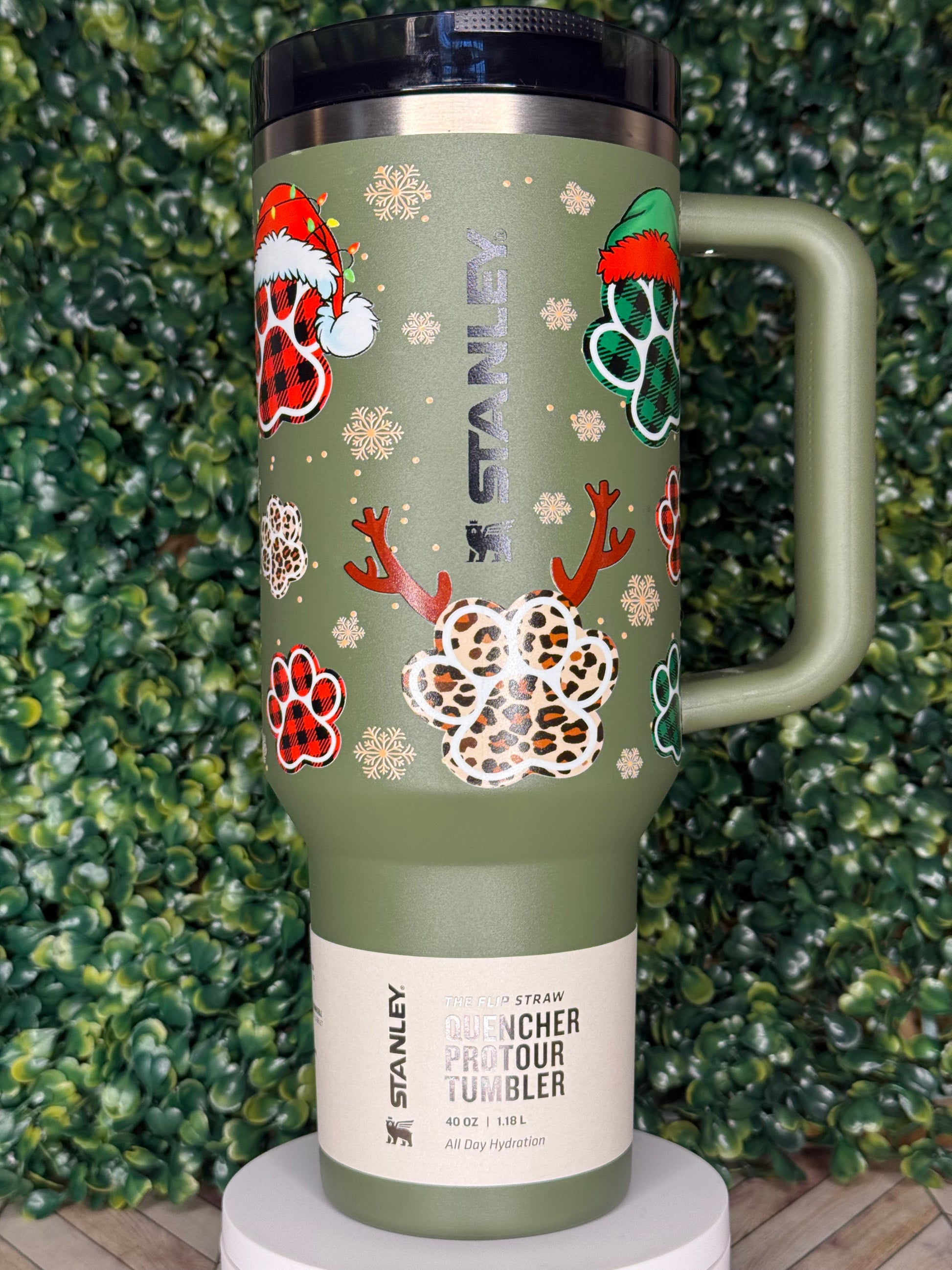 A green insulated tumbler with a handle, decorated with various Christmas-themed designs, including snowflakes, reindeer, and paw prints.